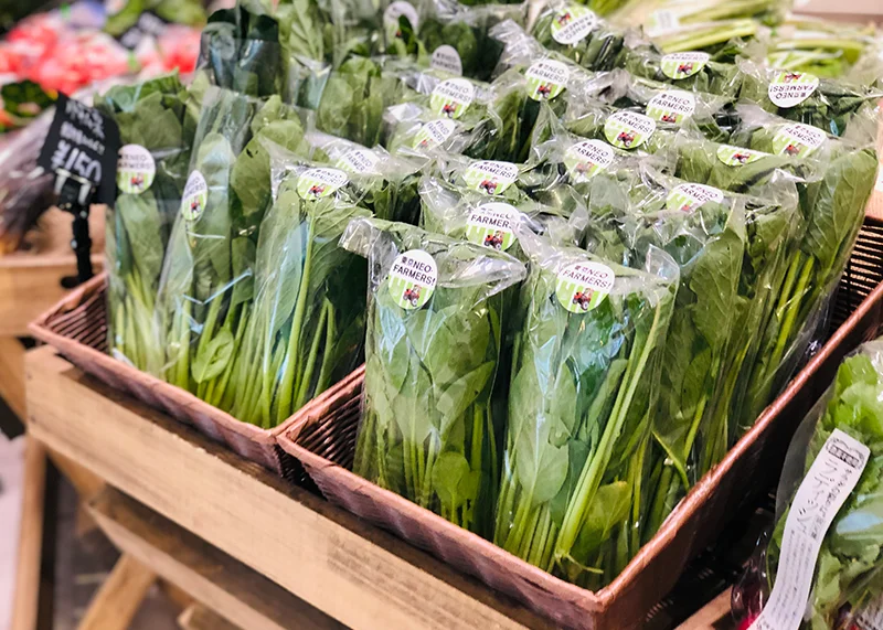 生産者シールが貼られた葉物野菜が、個包装でかごに並んでいる。取扱商品カテゴリー「葉茎菜類（キャベツ、ほうれん草、レタスなど）」の売り場写真である。